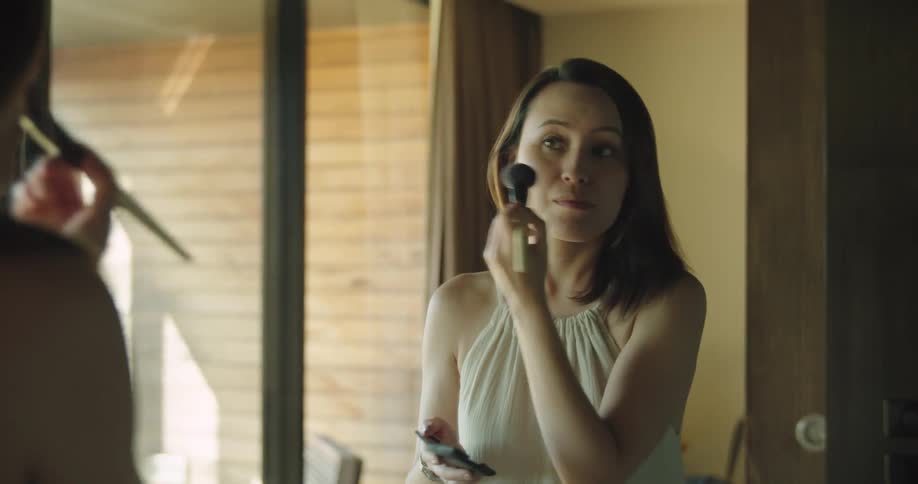 Woman facing mirror near sliding glass door puts on makeup
