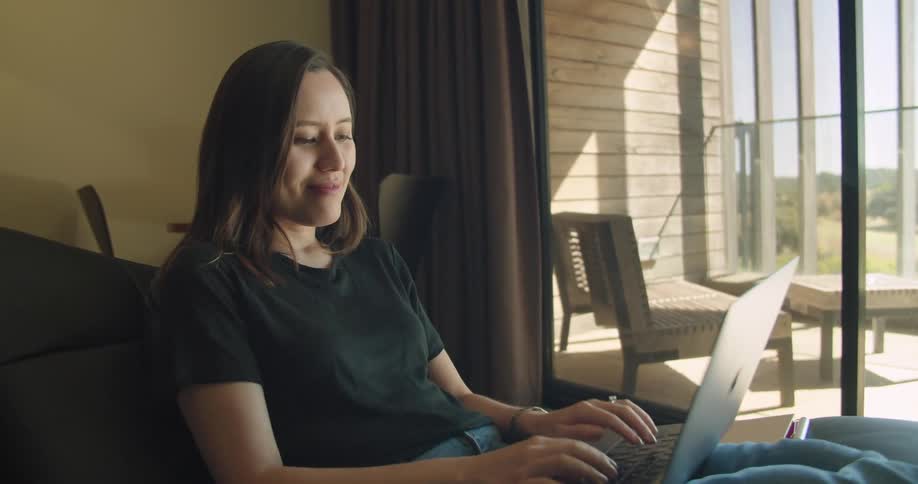 A woman is sitting in a room and typing on a laptop