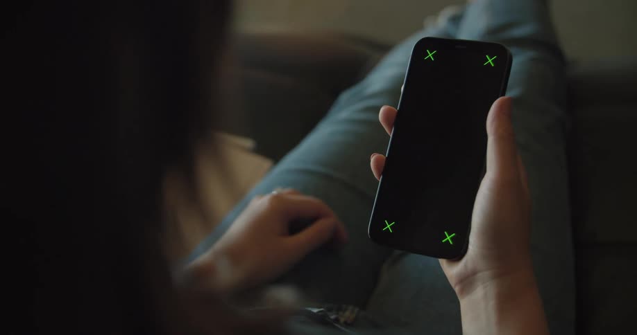 A teenage girl sitting on a couch picks up her cell phone and looks at the greens xs on each corner