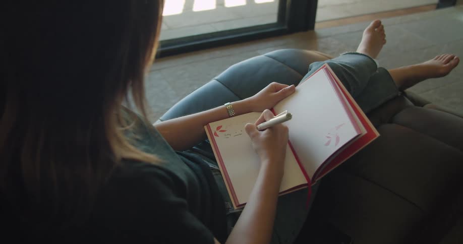 A woman is sitting on a chair indoors and writing in a journal