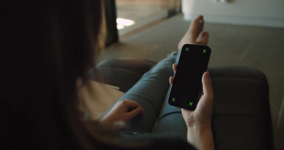 A woman in a room sitting on a couch looking at a smart phone