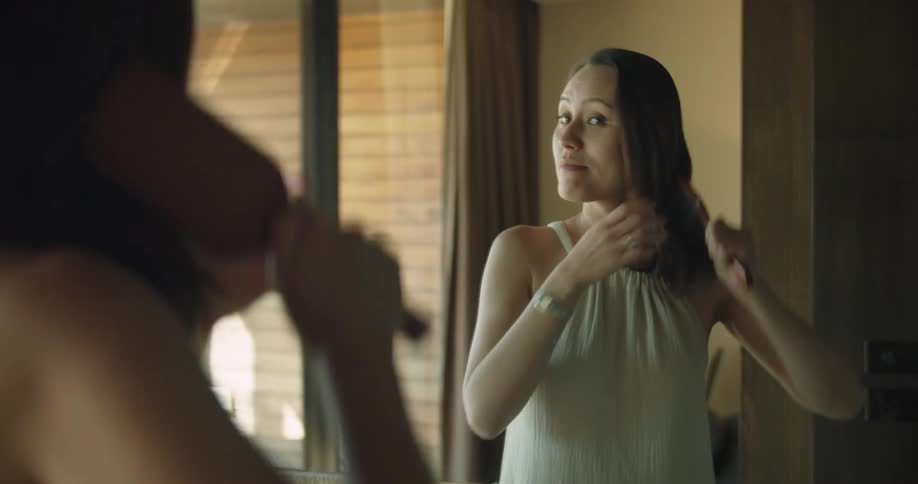 A woman smiles softly as she brushes her hair in the mirror