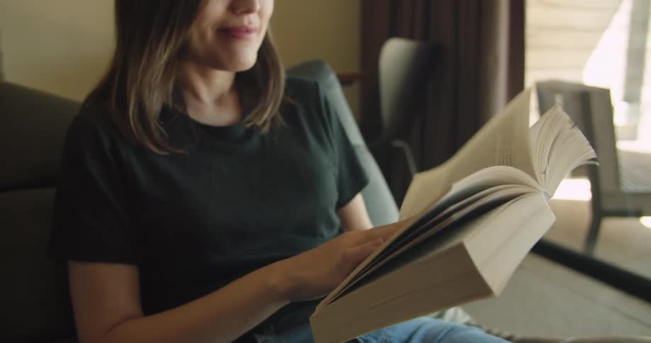 Woman leisurely reading a book sitting on a chair in the livingroom at home