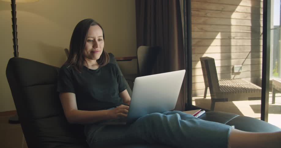 A woman sits at home with a laptop in her lap and then opens it up and starts typing