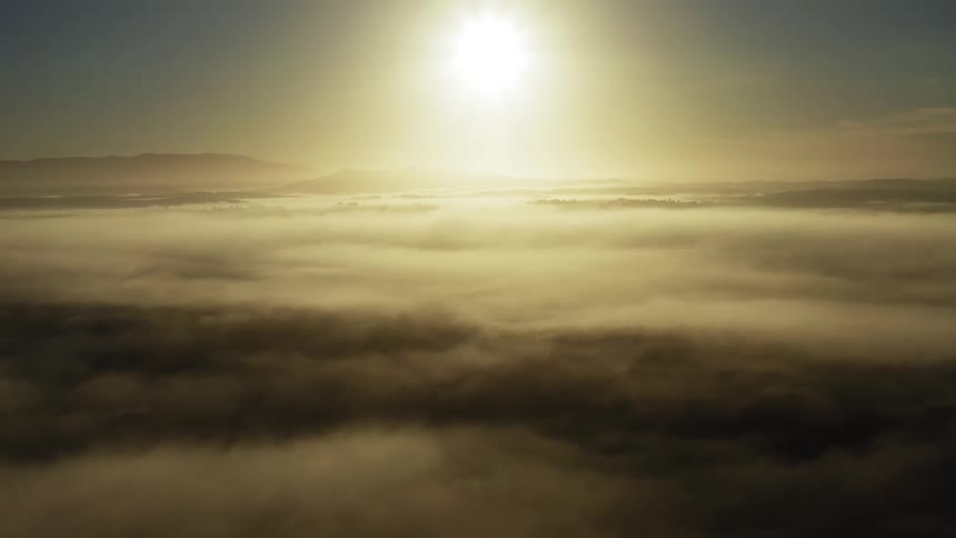 Bight sun shining above the clouds with mountains on the distant horizon