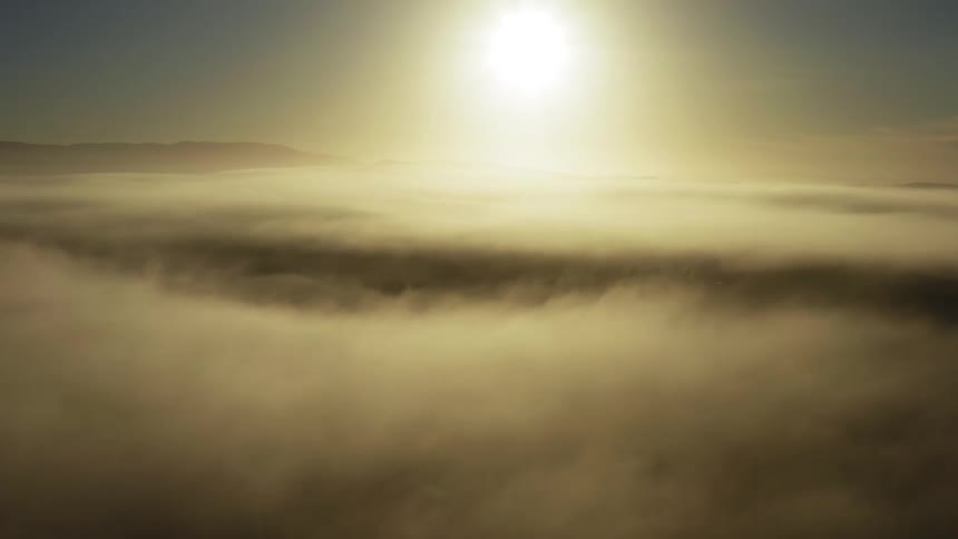 Aerial view of the sun setting over the clouds near the mountains