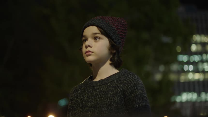 Person with beanie and grey pullover looks around at night