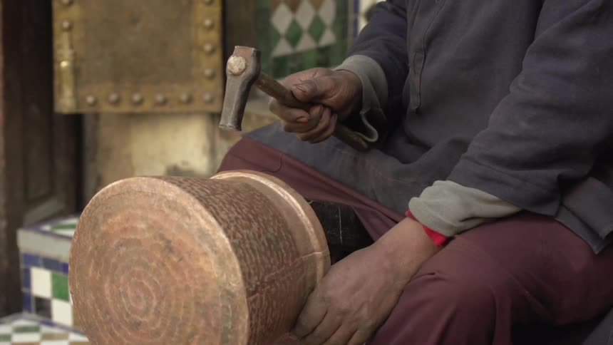 A man is hammering a drum near his lap