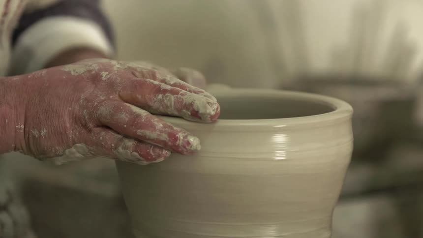 Hands add water to the clay on a potters wheel as they shape the clay
