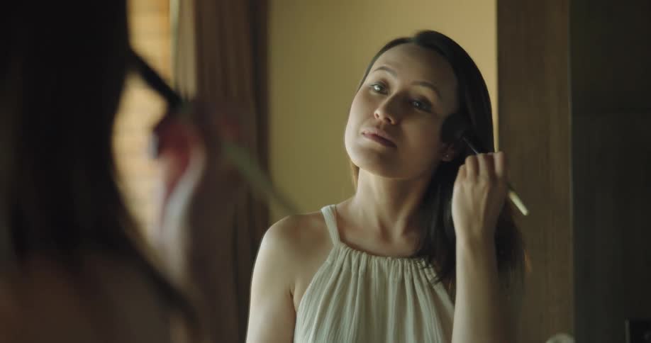 Young woman applies makeup with a brush in front of a mirror in a room at home