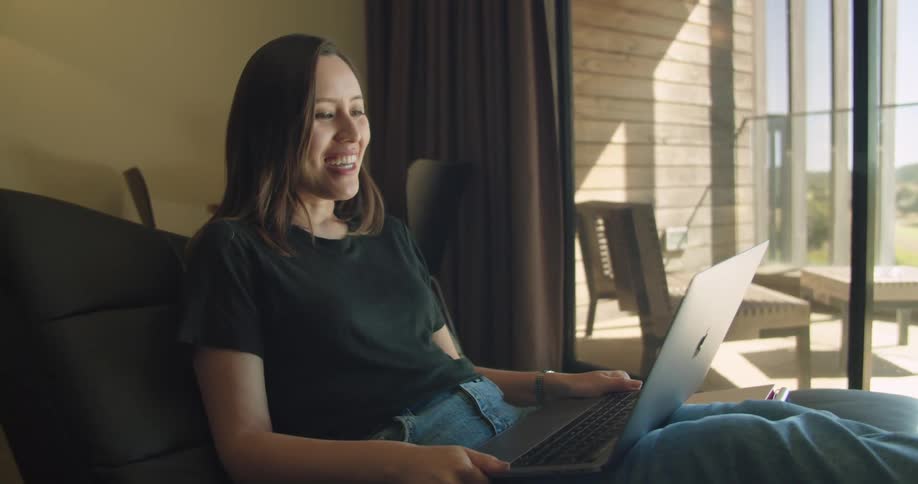 A woman smiles and waves to someone during a video call on her laptop