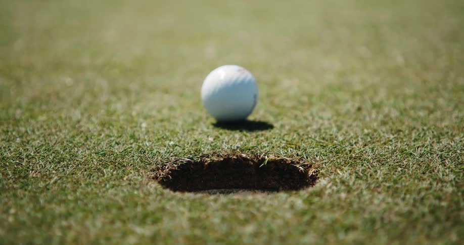 A close up of a golf ball going into a hole