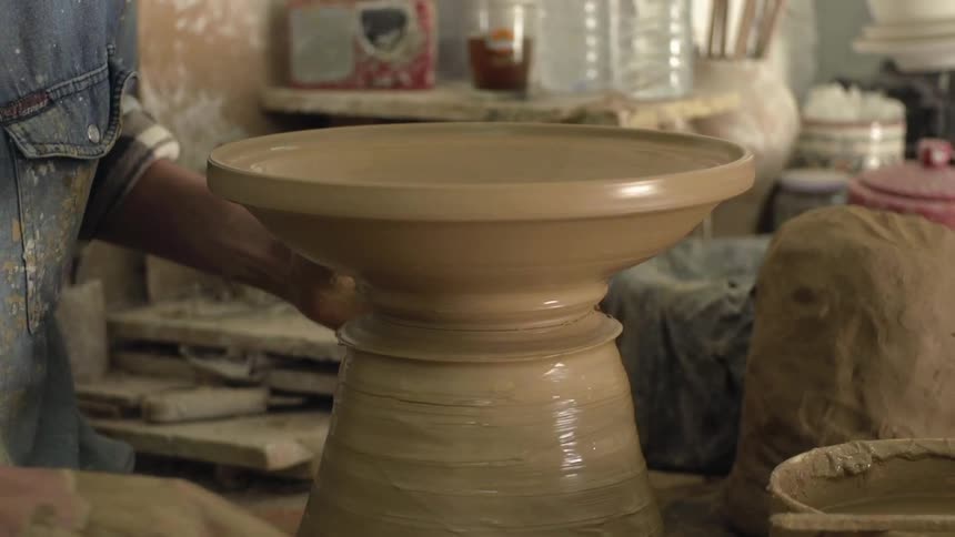 A person is making pottery indoors during the day