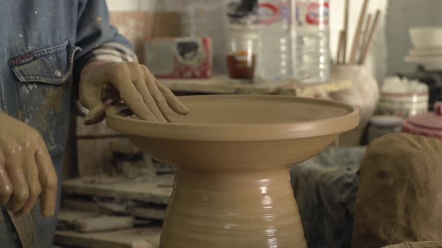 A woman carefully shapes a vase out of clay that is spinning atop a pottery wheel