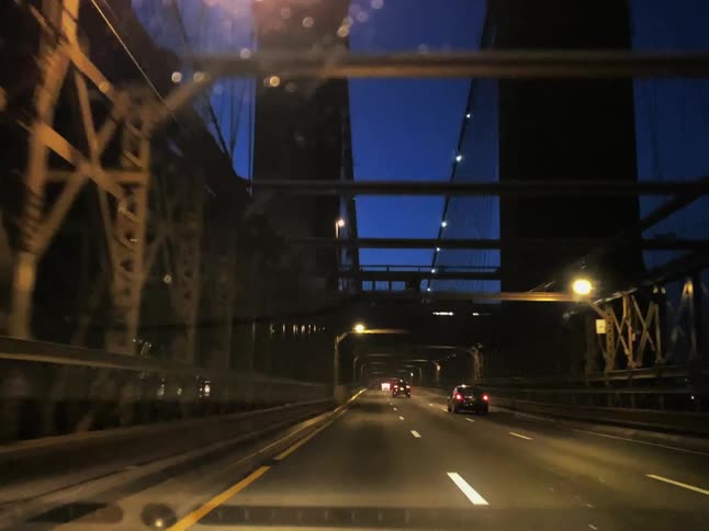 Street lights glow and a beacon flashes on a bridge as cars travel across