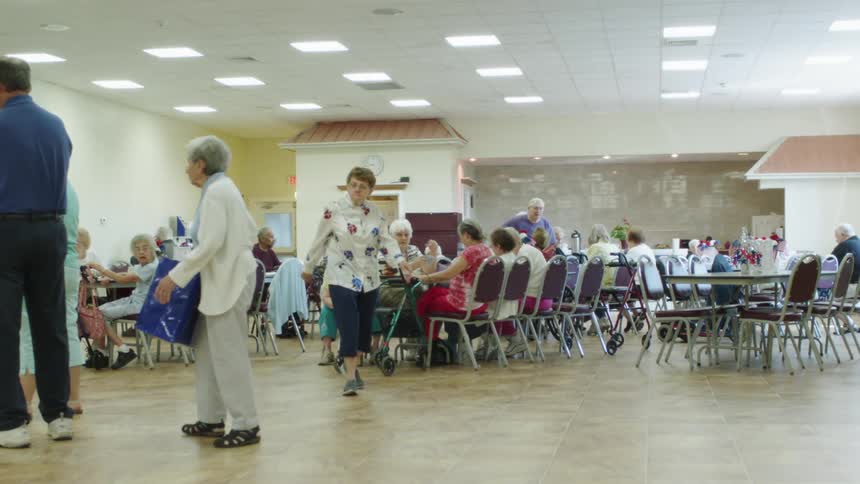 Elderly people walking and sitting in a room with tables and chairs