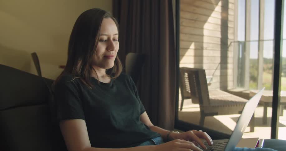 A woman is typing on laptop while sitting in her room