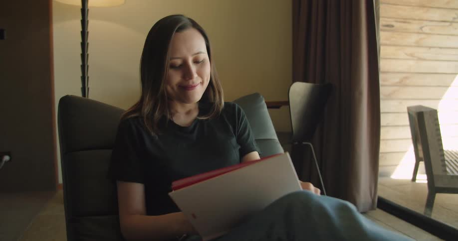 Young woman taking notes in a notebook while sitting on a chair in the living room