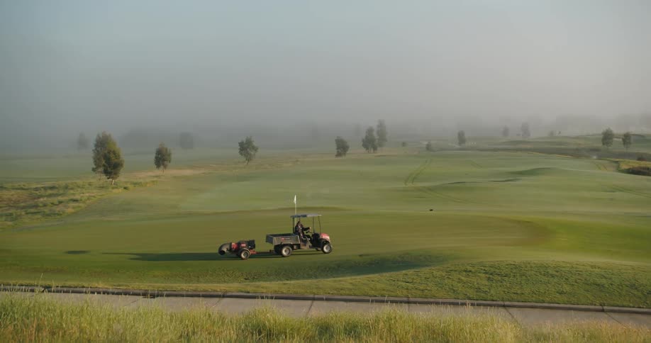 A golf course at midday with a golf cart driving