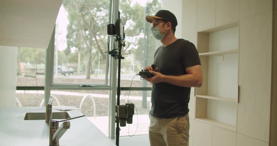 A man in a mask looks at a camera screen and holds controls