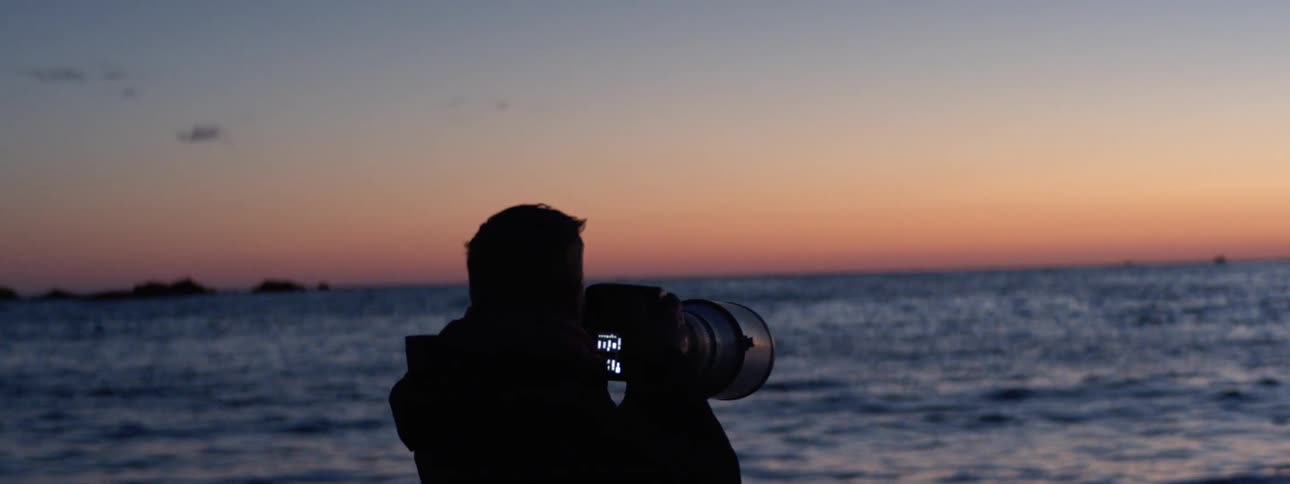 While the sun is below the horizon a photographer aims his camera at the horizon