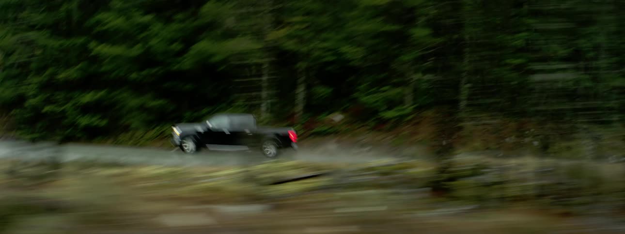 Black truck speeds along highway through forest past mountain slope splashing water when it drives through puddles