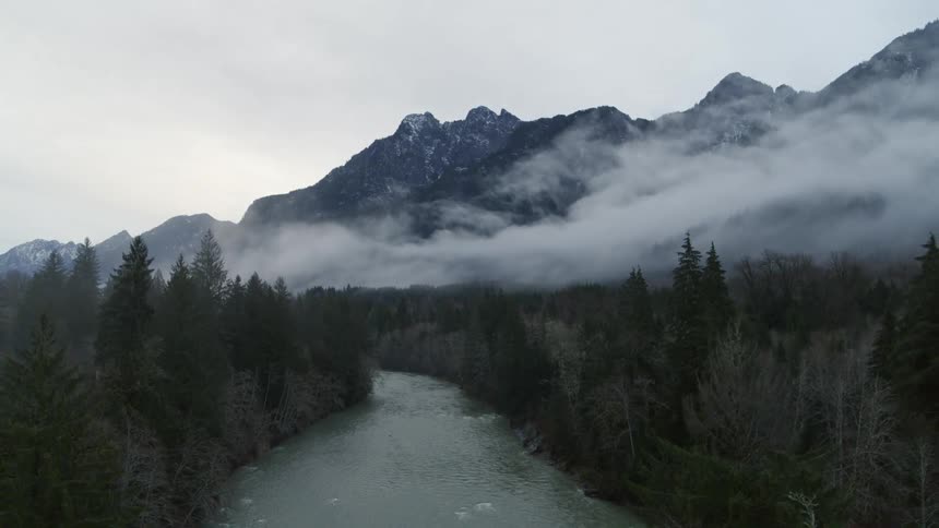 Pullback ascent along a mountain river running through a fog shrouded forest