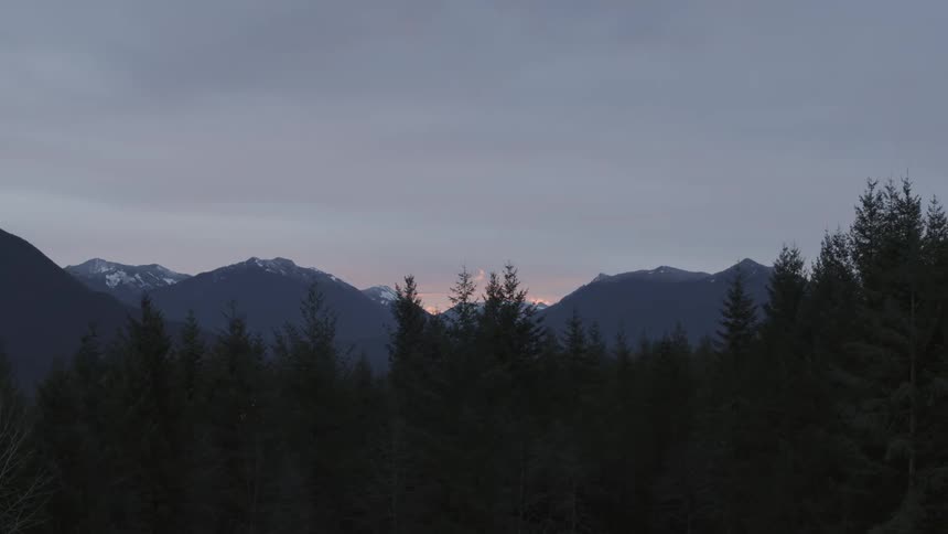 Traversing along tree tops as the first morning light peeks out from behind mountains on the horizon