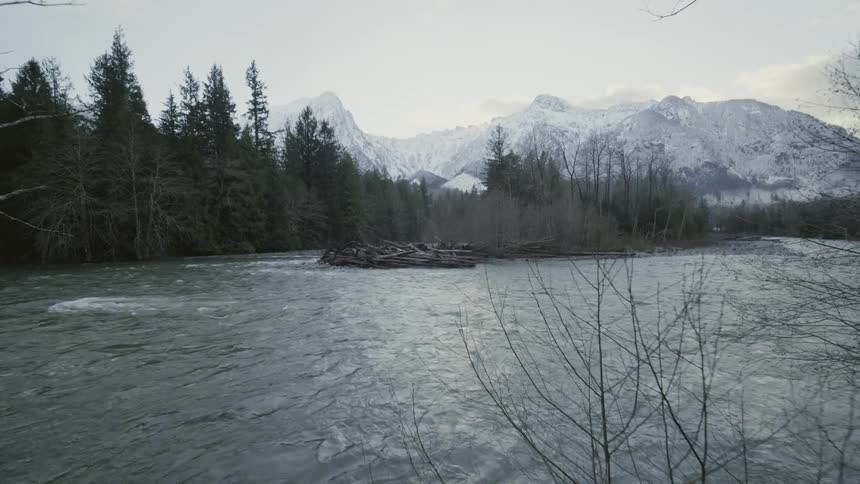 A cold glacial river flows at the base of snowy mountains