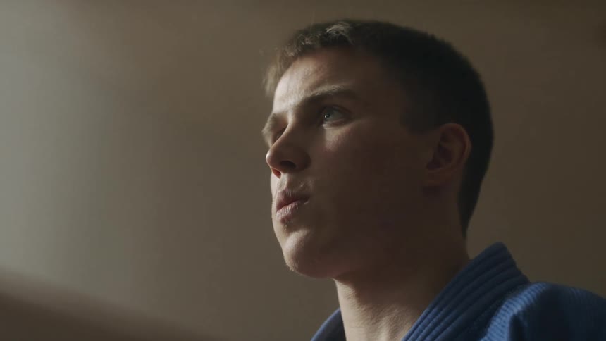 A young man in a martial arts uniform slowly exhales air as he raises his head