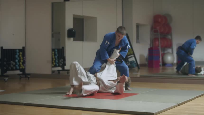 Two men are sparring as one is tossed to the ground