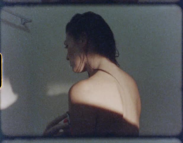 A woman stands and undresses in a shadow