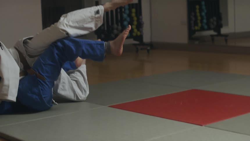 Man with white judo suit throws man wearing blue judo suit to the ground