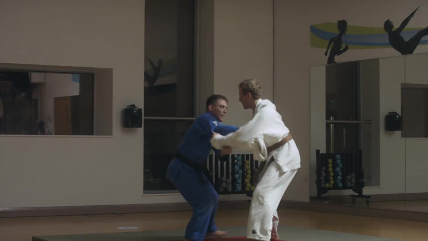 Two men in a room on a mat practicing martial arts with gi and belts
