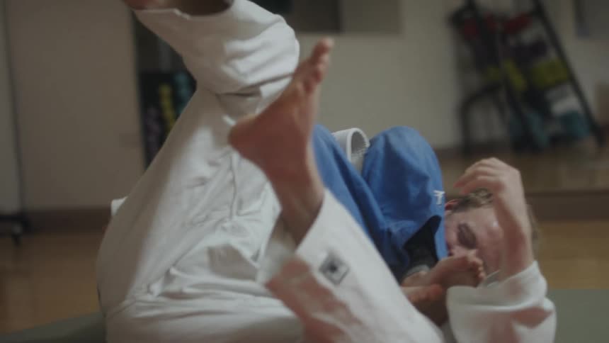 Two judokas fighting on the floor of a gym in front of a mirror