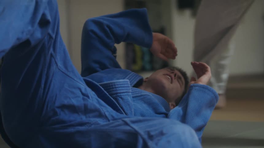A man winces in pain after being slammed on the ground during a karate match