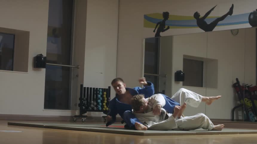 Two people with judo suits fight using their arms and legs and hands and feet in the gym