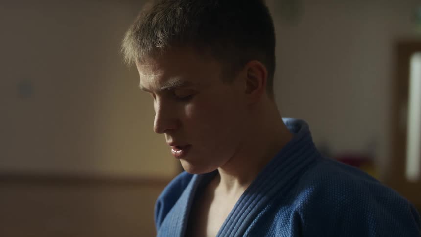 Tired young man wearing a blue judo uniform breathing with eyes closed inside a dimly lit room