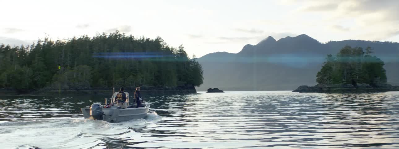 Photographer rides a boat on a lake near small islands with pine trees near the mountain