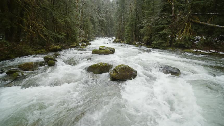 Pullback descent reveal of mossy river rocks and churning whitewater rapids