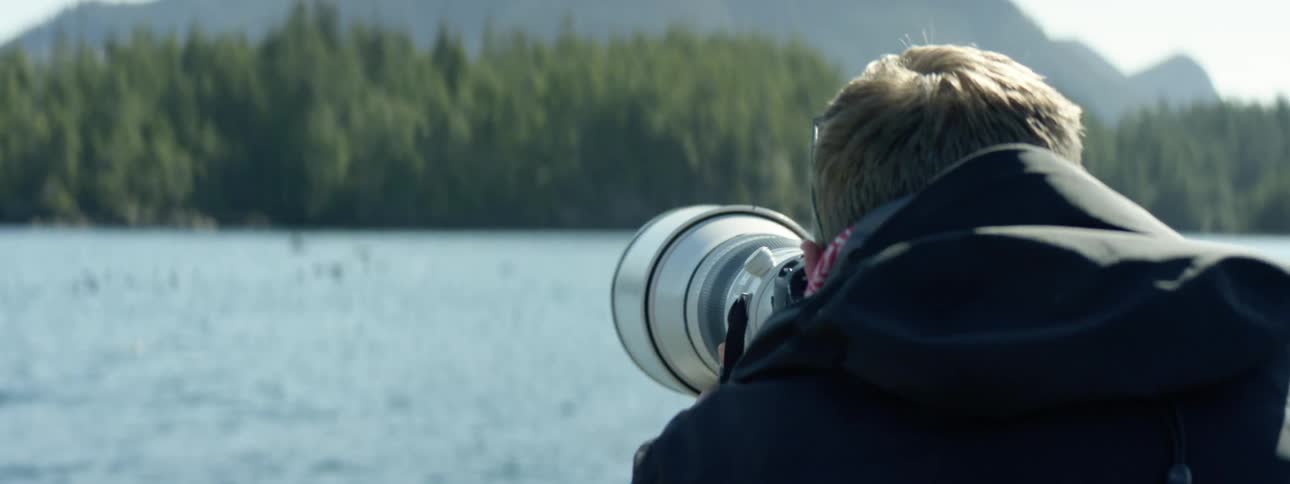 Photographer following birds with the long focus lens of a camera over a lake in the forest