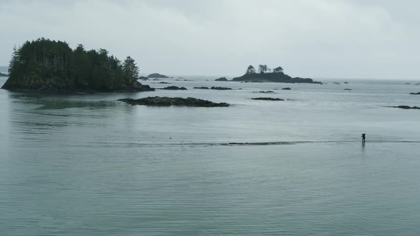 Aerial view of cameraman with backpack walks in sea water on cloudy day