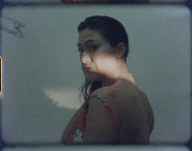 A woman stands touching her neck as she looks at the camera