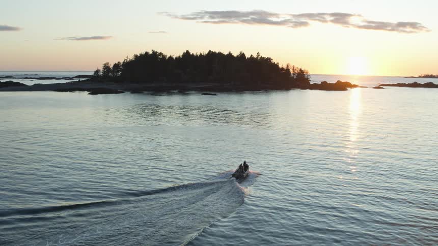 Two people on a boat sailing towards an island as the sun sets