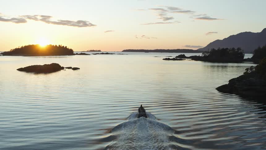 The sun rises over the island trees on the horizon as a motor boat leaves a wake in the rippling water