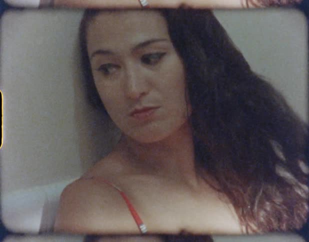 A woman with long hair and wearing a red printed top sites on a white chair