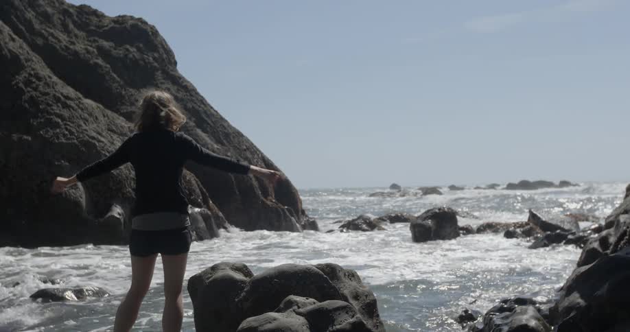 A woman is standing in the water near a beach waving her arms up then down