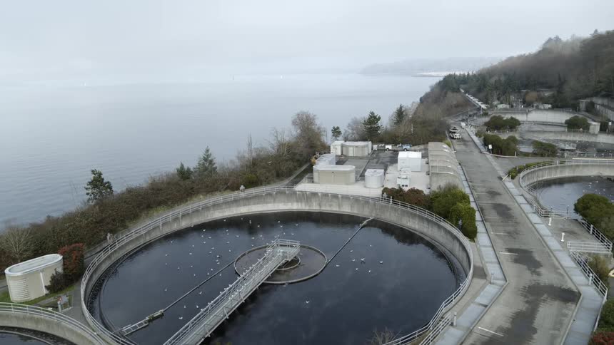 Pullback reveal of wastewater tanks and pump equipment at a sewage treatment plant along an inland bay