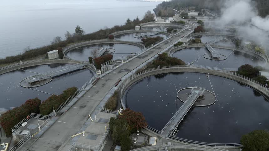 Flying over circular sewage tanks at a wastewater management and treatment plant near the ocean