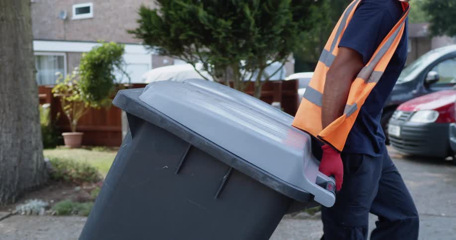 A waste collector or garbage man pulling garbage bins through the street